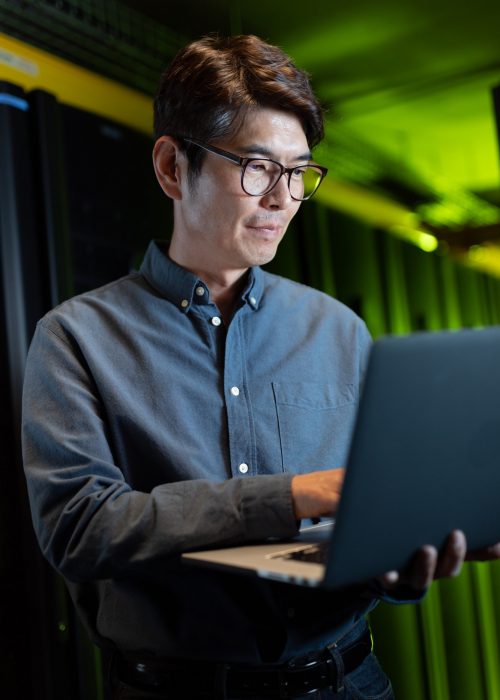 Asian male engineer using laptop in computer server room